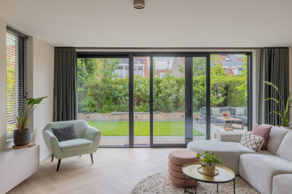 Grote antraciet schuifpui in een moderne woonkamer met uitzicht op een groene tuin.